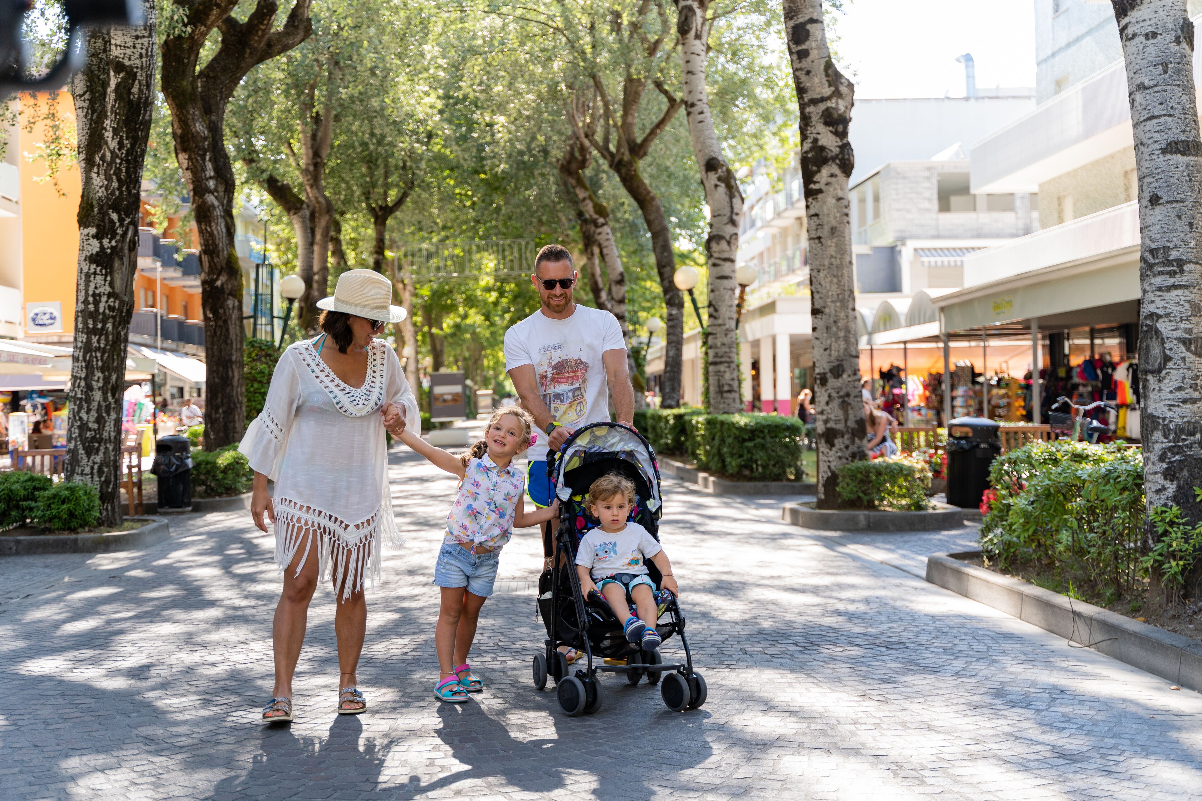 A family walking down a tree-lined street with shops on the right.