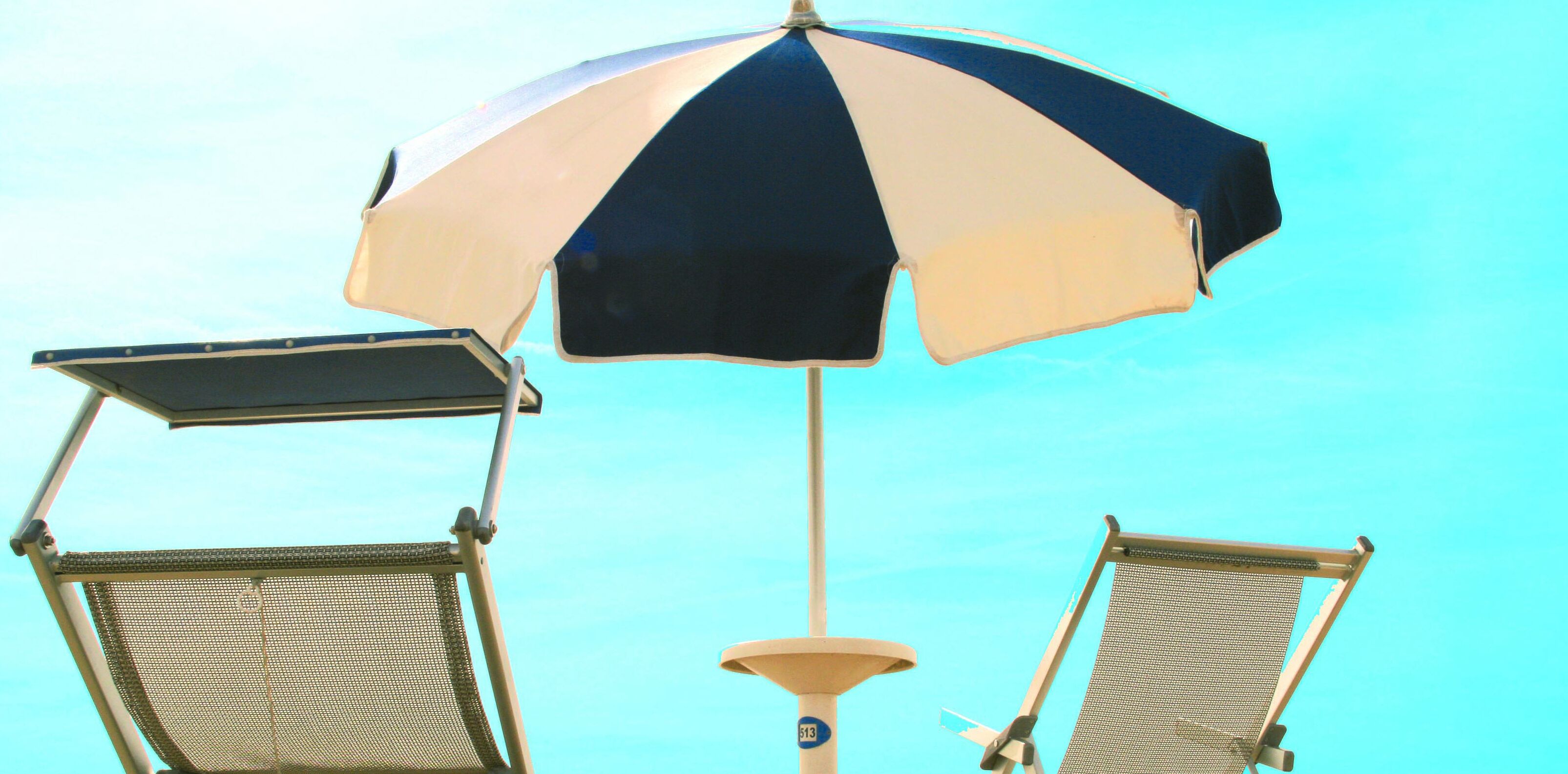 Una sombrilla de playa, dos sillas de playa y un cielo despejado.