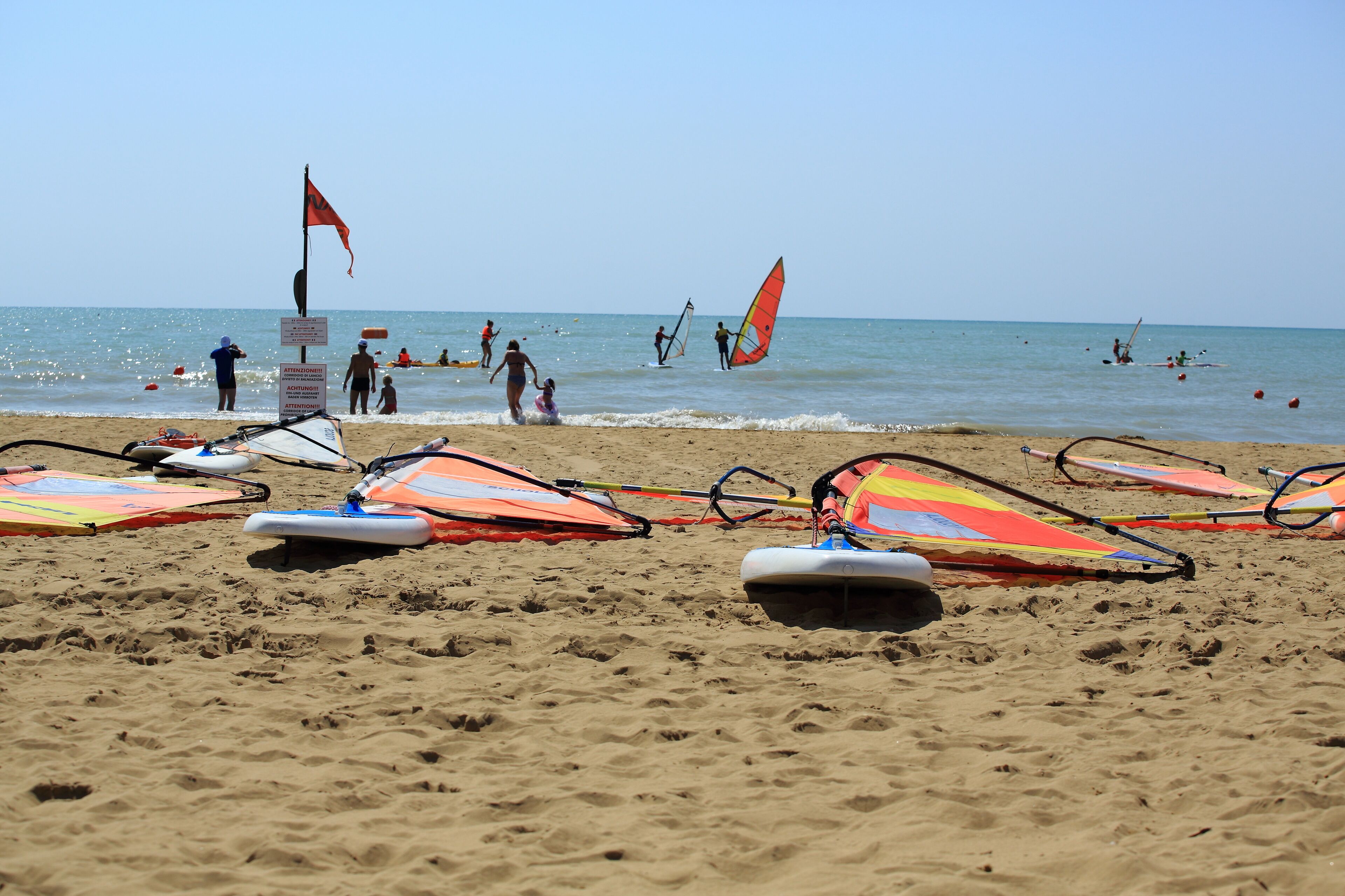 A sandy beach with windsurfing equipment and a flag.