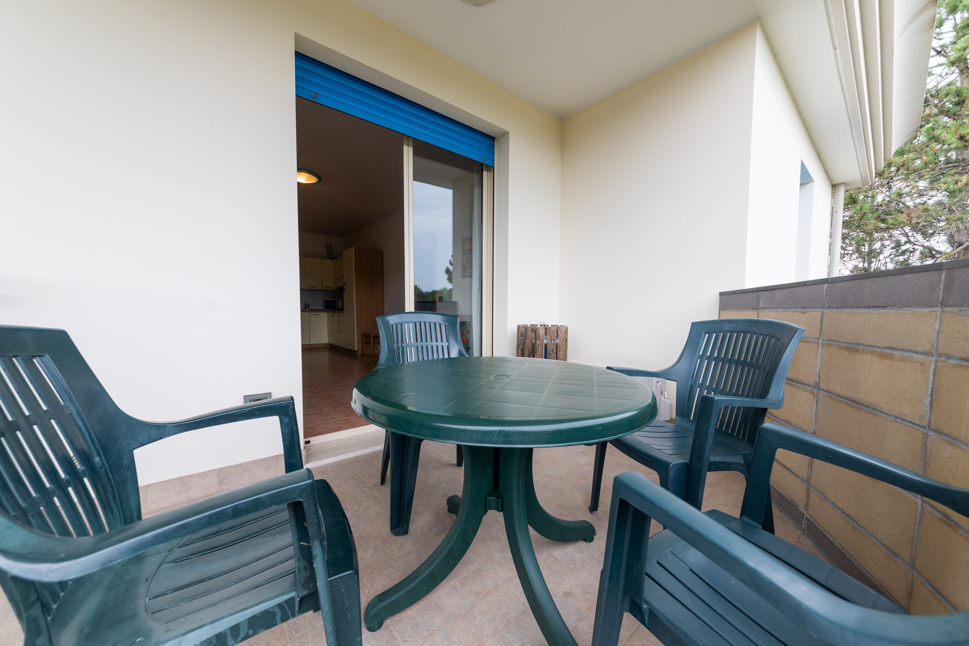 Ein Balkon mit einem runden Tisch und vier Stühlen, eine blaue Tür und Blick ins Innere.
