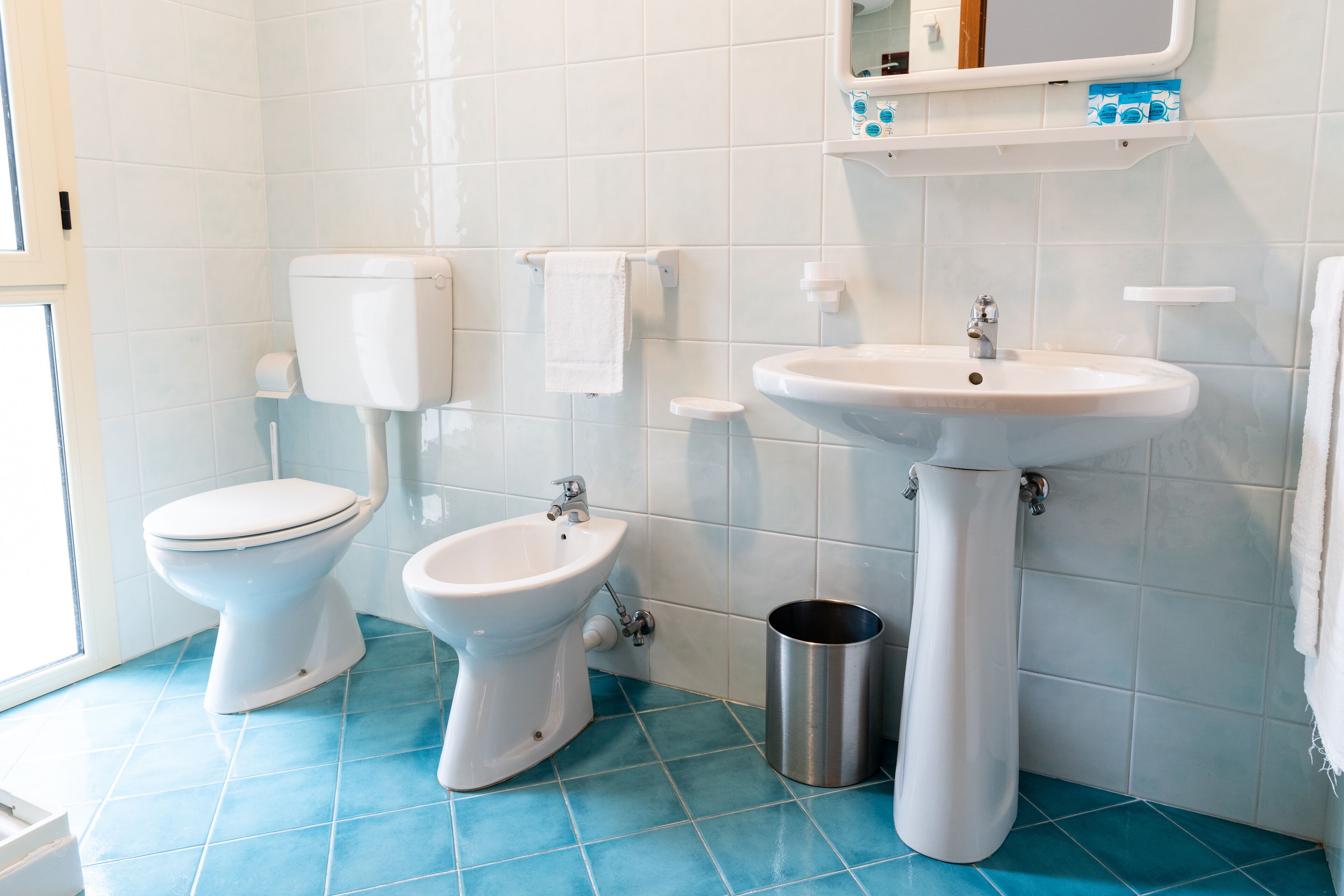 A bathroom with a toilet, bidet, sink, and a trash can.
