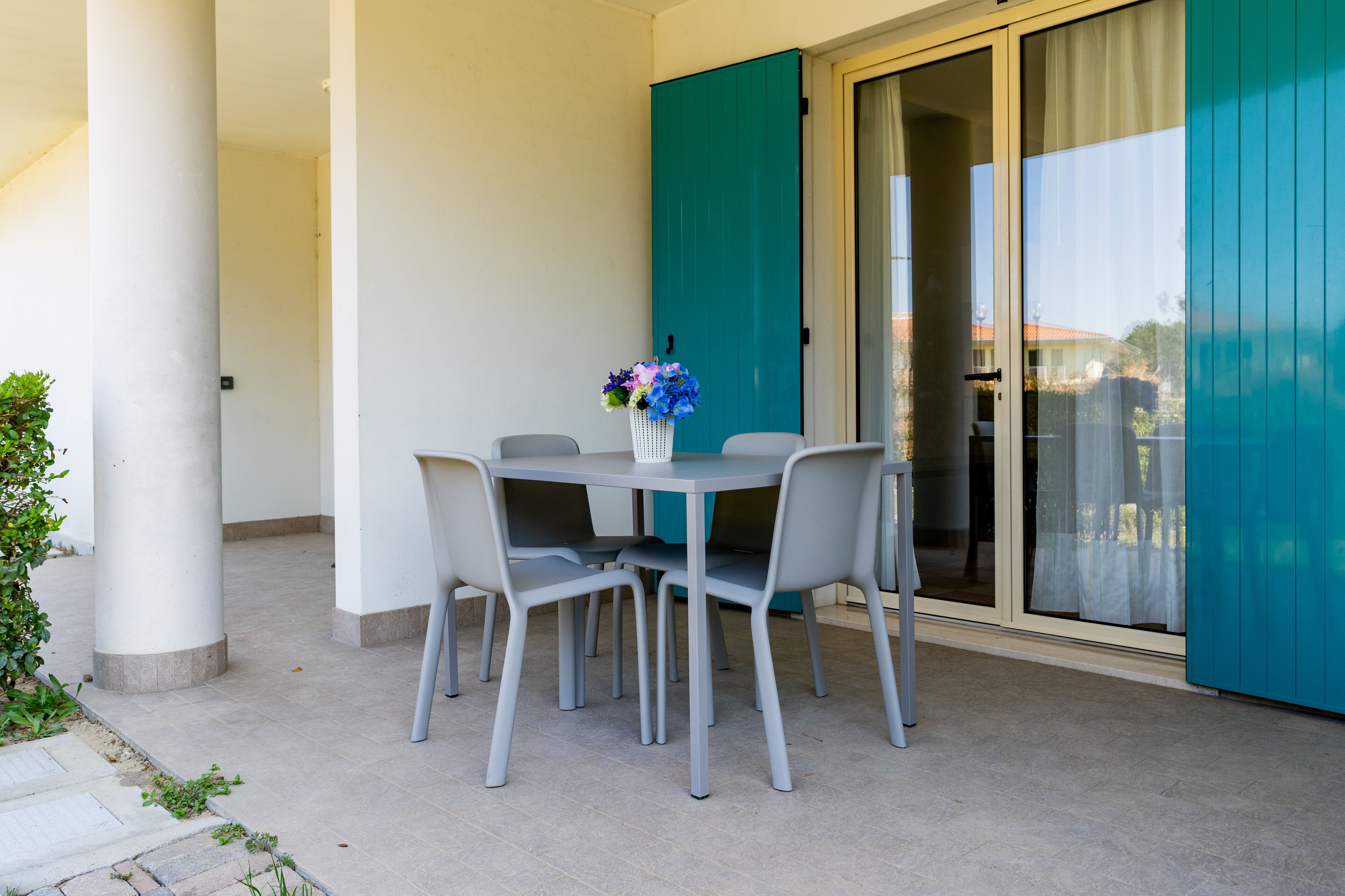 A balcony with a table and chairs, a vase with flowers, and a sliding glass door.