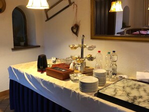 A buffet setup with a coffee maker, a fruit bowl, and stacked plates on a table.