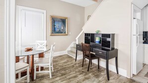 A dining area with a glass table, white chairs, a black desk with a computer, and a staircase leading to another room. - Duval Dream Loft - On Duval street (Key West)