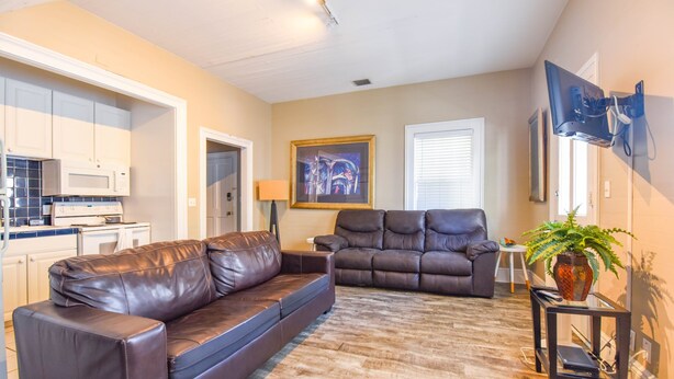 A living room with a brown leather sofa, a brown recliner, a small table with a plant, and a flat-screen TV mounted on the wall. - Duval Dream Loft - On Duval street (Key West)