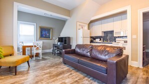 A living room with a brown leather sofa, a dining table with chairs, a kitchen with white cabinets and blue tiles, and a staircase leading to another level. - Duval Dream Loft - On Duval street (Key West)