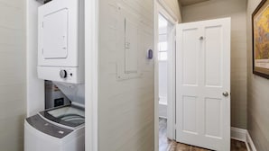 A laundry room with a front-loading washer and dryer, a door with a handle, and a wall-mounted light switch.