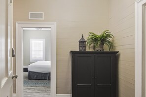 A hallway with a bed, a dark cabinet, and a potted plant. - The Collins - On Duval Street (Key West)