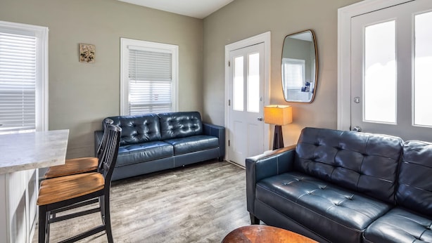 A living room with a dark leather sofa, a wooden coffee table, and a dining area with a white countertop.