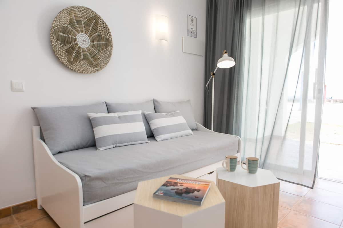 A modern living room with a grey sofa, striped cushions, a round woven wall art piece, a floor lamp, and a small table with a magazine and two mugs.