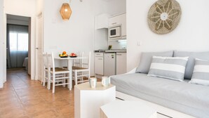Ein modernes, helles Wohnzimmer mit grauem Sofa, einem Essbereich mit Tisch und Stühlen sowie einer Küche mit Mikrowelle.
