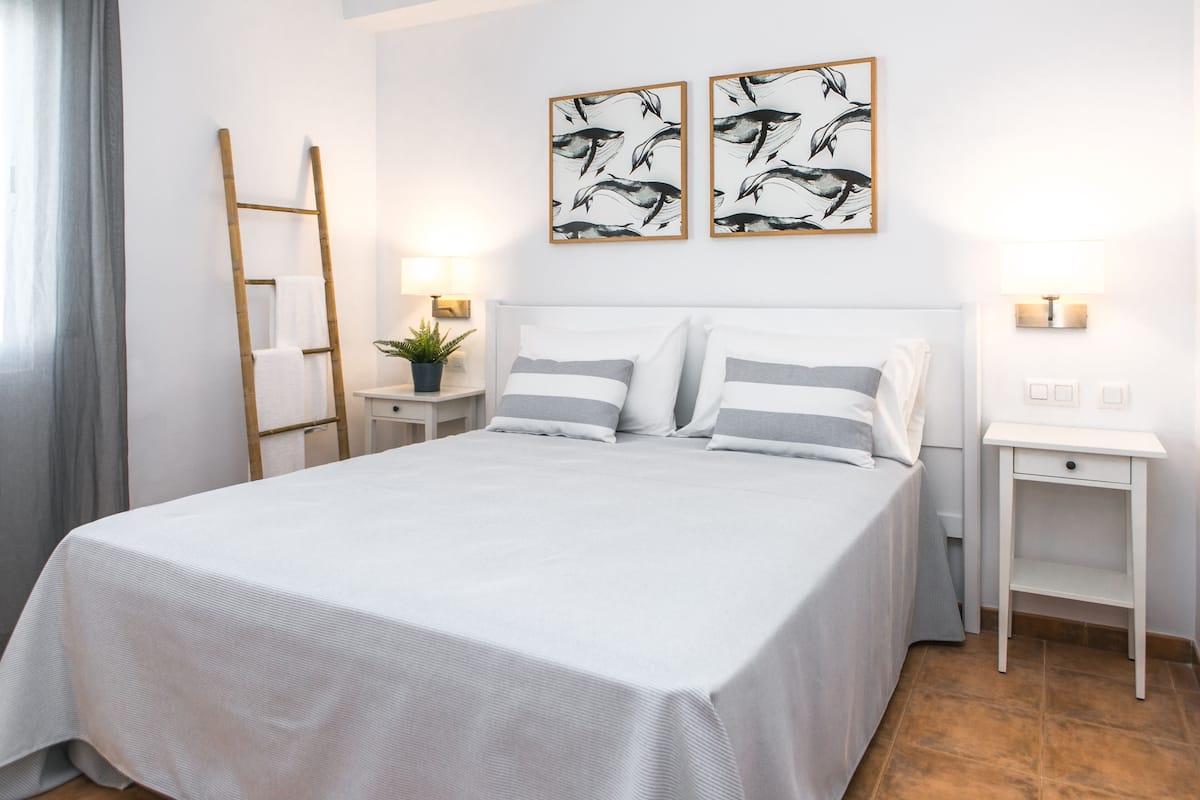 A neatly made bed with a white bedspread and two pillows, flanked by two bedside tables with lamps.