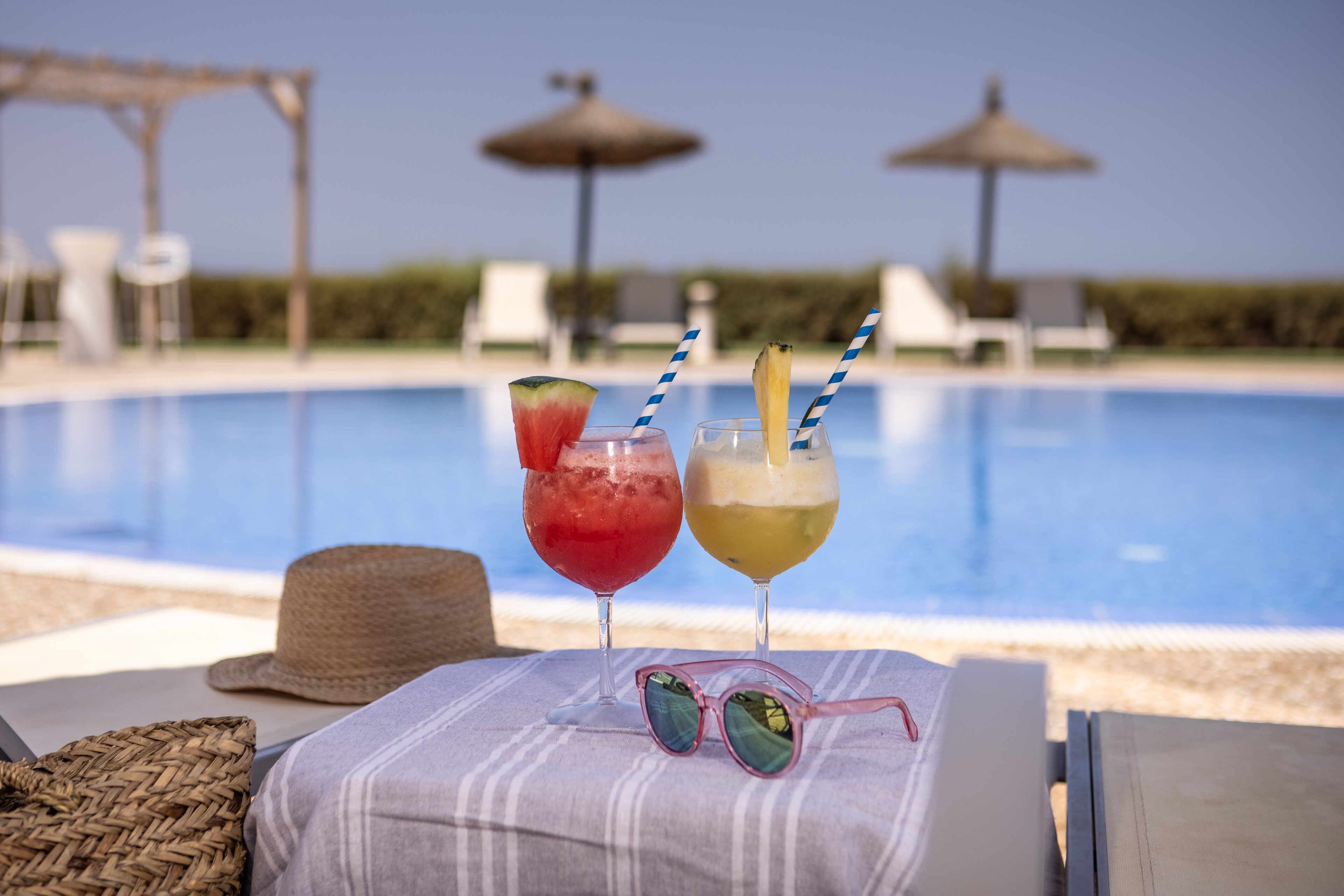 Ambiente de piscina com duas bebidas, um canudo e outro canudo com abacaxi à direita.