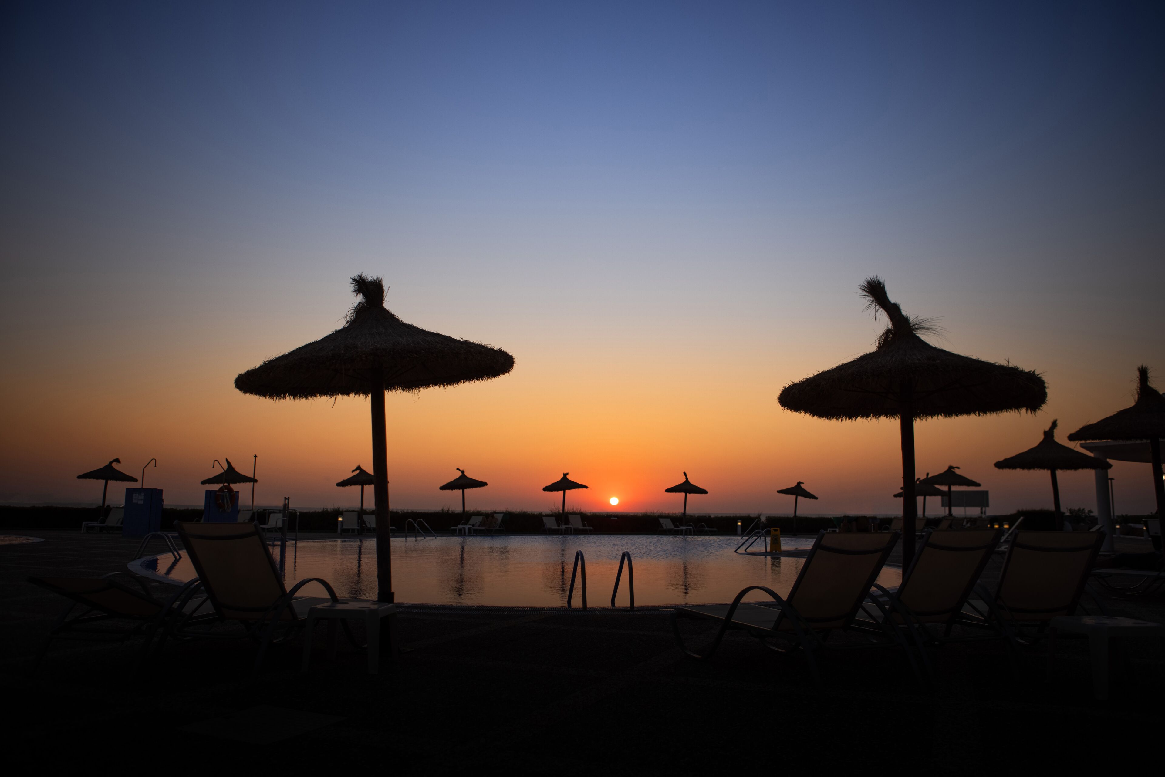 Zona junto a la piscina con sillones de descanso y sombrillas al atardecer.