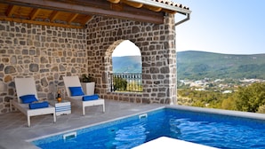A stone-walled infinity pool with two lounge chairs and a bottle of champagne, overlooking a scenic landscape. - Villa Dub (Kotor)