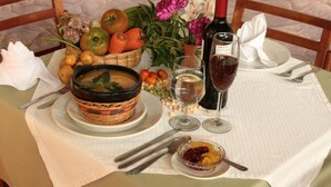A table set with a bowl of soup, a bottle of wine, a glass of white wine, a basket of fruits, and a small bowl of fruit preserves.