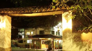 A building with a sign reading "Los Arrayanes" at night, featuring a covered entrance and outdoor seating area.