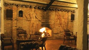 A cozy room with a brick fireplace, leather chairs, and a stone wall with carvings.
