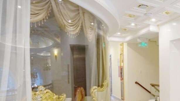 A luxurious room with a curved glass partition, elegant gold-trimmed furniture, and a polished marble floor.
