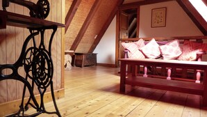 Une pièce avec un plancher en bois, une machine à coudre, un banc avec des coussins roses et un plafond en pente.