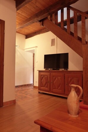 Een kamer met houten vloer, een televisie op een kast en een vaas op een tafel.