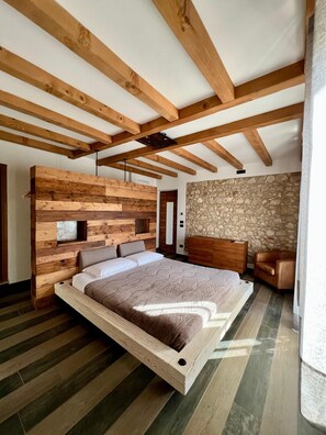 A modern bedroom with a wooden headboard, a stone wall, and a bed with a wooden frame. - Agriturismo Tamellini (Soave)