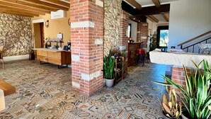 A spacious lobby with a patterned tile floor, wooden beams on the ceiling, a stone wall, and a brick pillar.