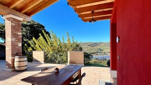 An outdoor patio with a wooden table and chairs, a red wall, and a view of the countryside.