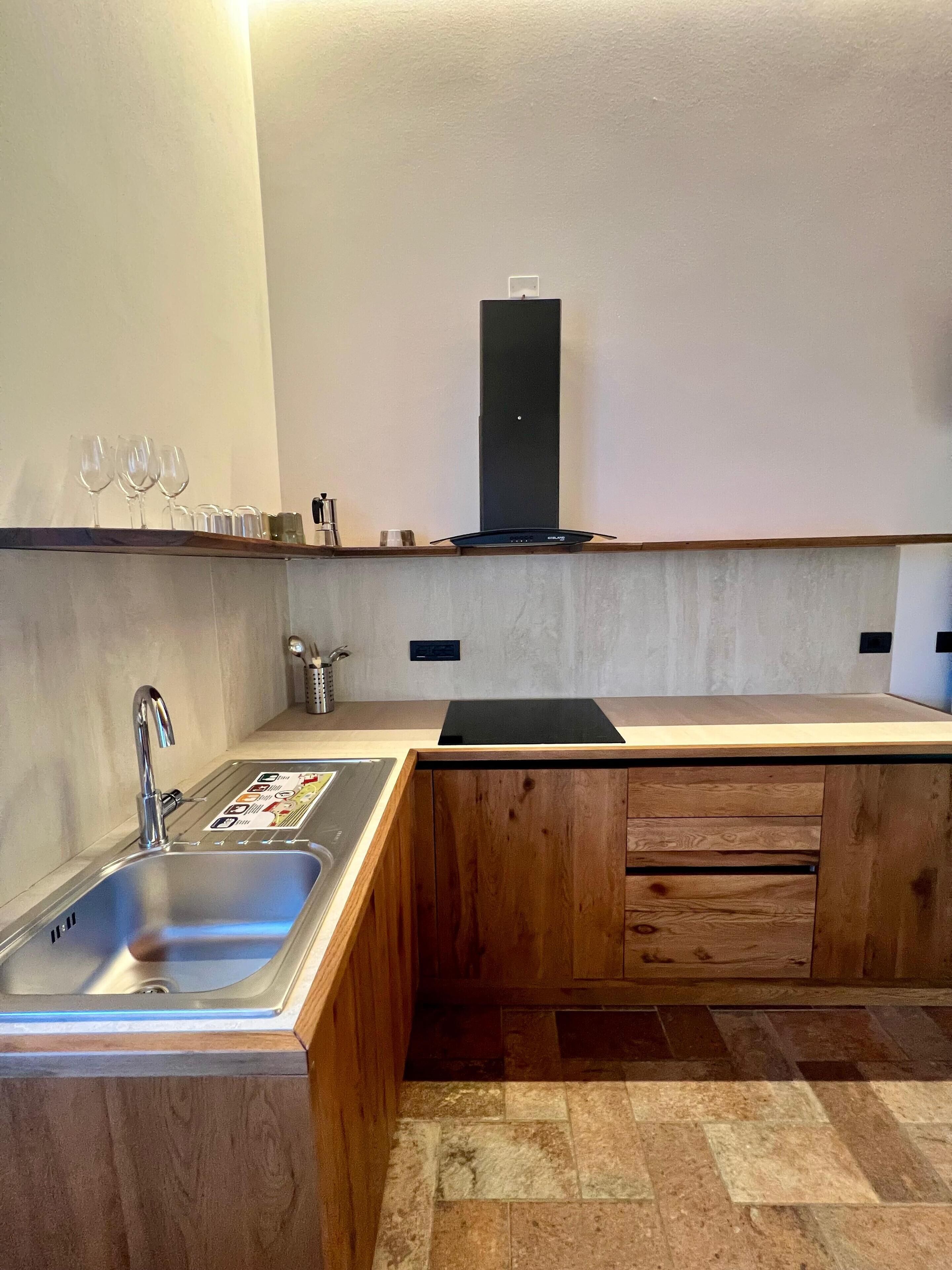 A modern kitchen with a stainless steel sink, wooden cabinets, and a black range hood.