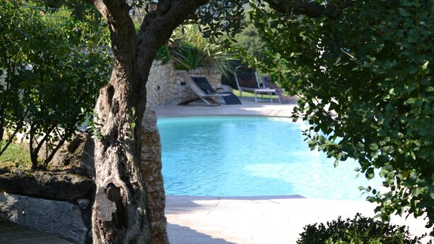 A pool area with lounge chairs and a stone wall in the background.