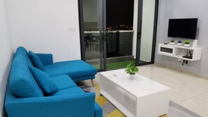Un salon moderne avec un canapé bleu, une table basse blanche et un téléviseur posé sur un meuble blanc.