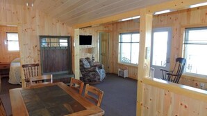 L’intérieur d’un chalet en bois comprend une table à manger, des chaises, un téléviseur et un coin salon avec fenêtre.