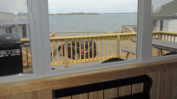 Une vue depuis une fenêtre donnant sur une terrasse en bois, avec un barbecue et un chien.