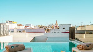 Un espace piscine aménagé sur le toit, offrant une vue sur le panorama urbain, notamment sur le clocher imposant d’une église.