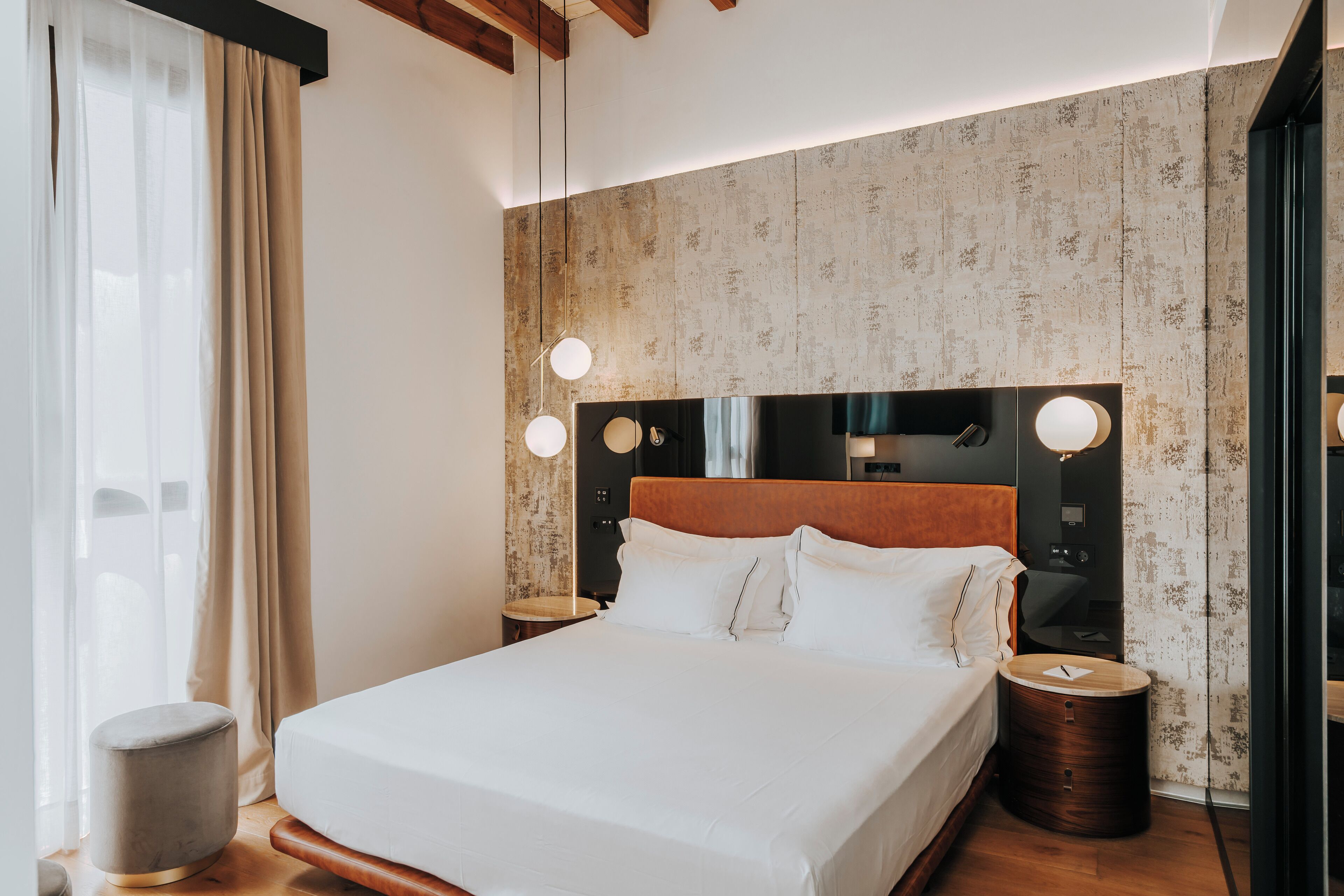 Une chambre d’hôtel moderne avec un grand lit, une tête de lit en bois et deux tables de chevet dotées de lampes rondes.