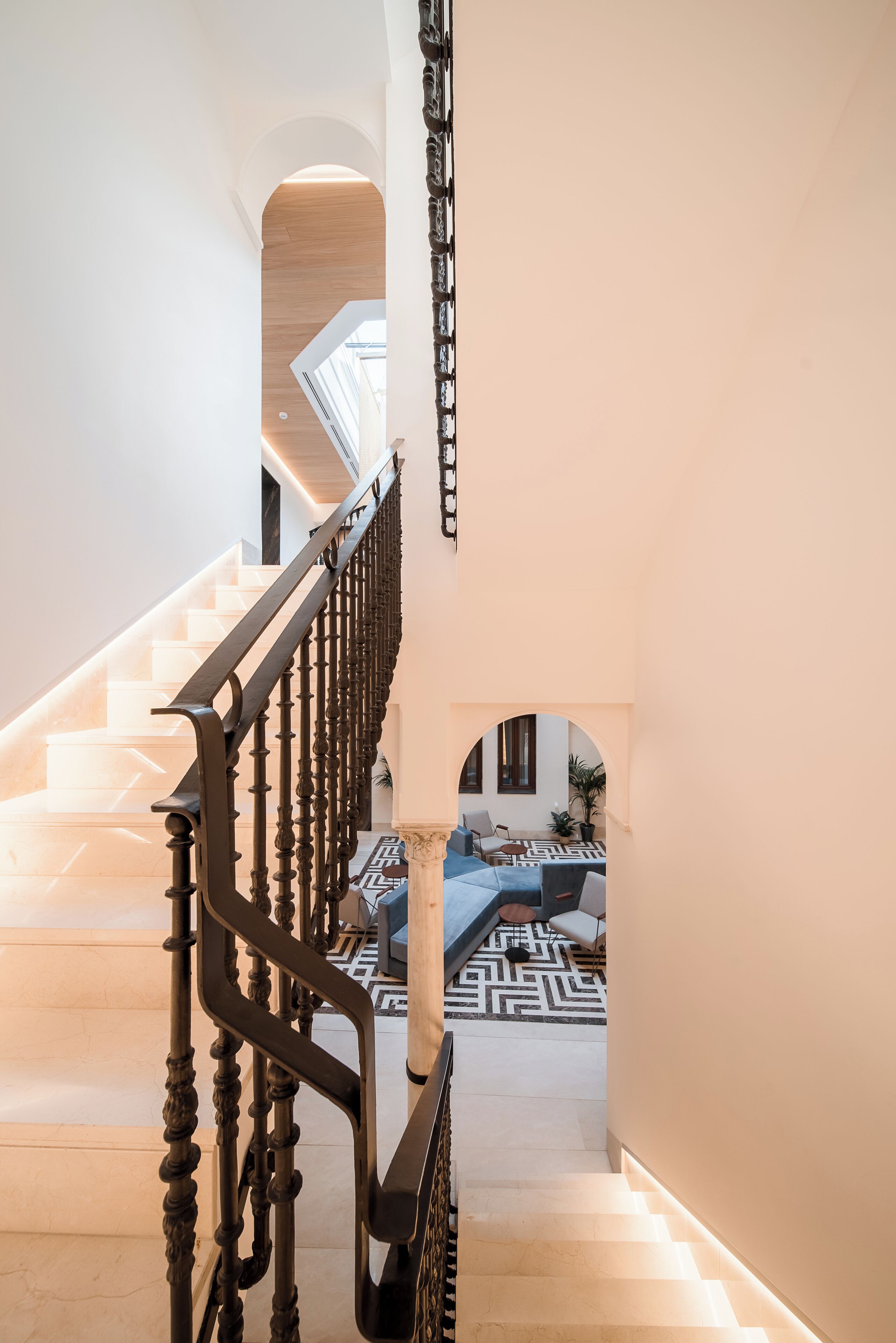 A staircase with ornate black railings leading to a living area with a patterned rug and a sofa.