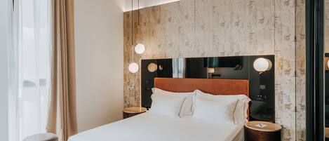 A modern hotel room with a large bed, wooden headboard, and round bedside tables.