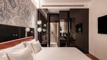 A modern hotel room with a large bed, a walk-in closet, a bathroom with a mirror and sink, and a television mounted on the wall.
