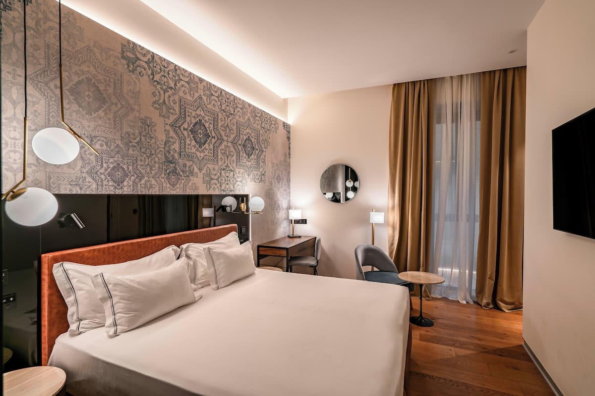 Una habitación de hotel con una cama grande, un escritorio, una silla, un televisor y un papel tapiz estampado.