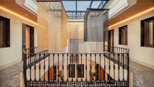 Un intérieur moderne avec un plafond en verre, un escalier en fer forgé noir et un atrium central agrémenté de plantes.