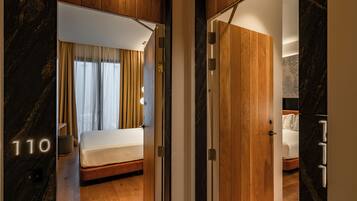 Habitación de hotel con cama, paneles de madera, pared de mármol con un número y vista a otra habitación.