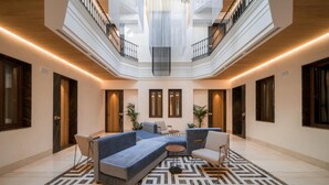 Un vaste atrium au design moderne, comprenant un espace de détente central avec des canapés et des fauteuils, un tapis à motifs et un haut plafond laissant entrer la lumière naturelle.