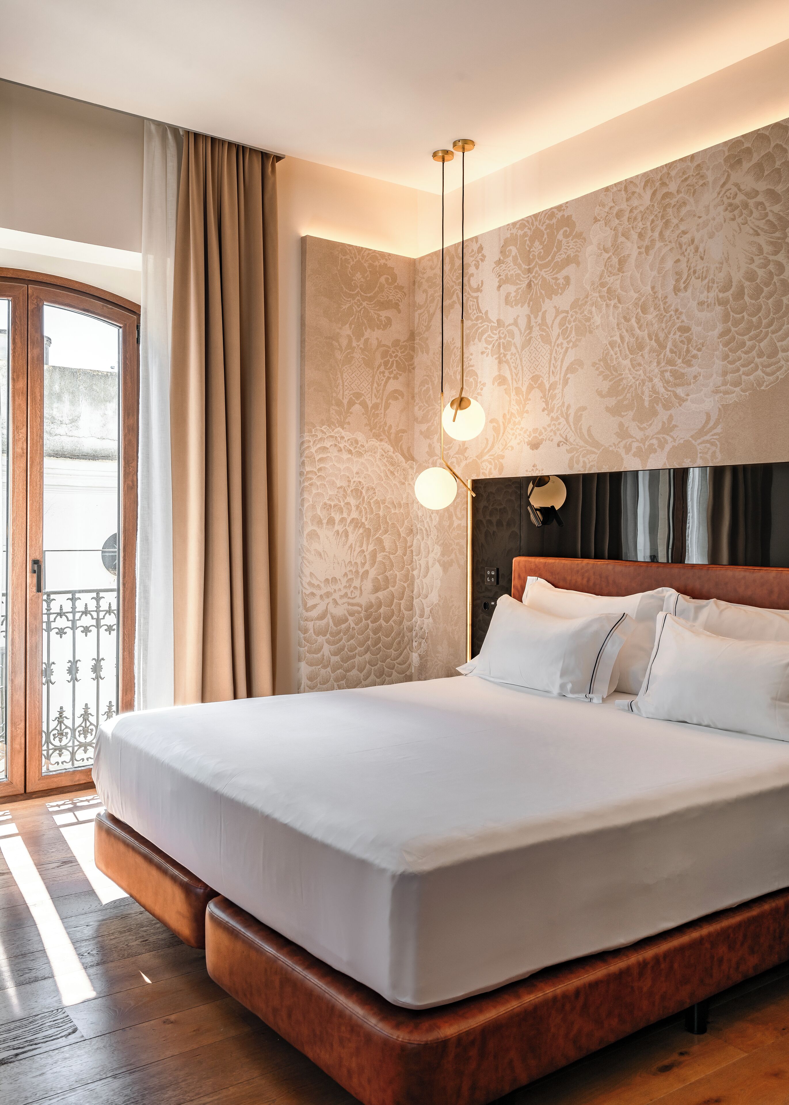 Une chambre d’hôtel avec un grand lit, une tête de lit en bois, un mur décoré d’un motif et une vue sur l’extérieur grâce à une porte vitrée.
