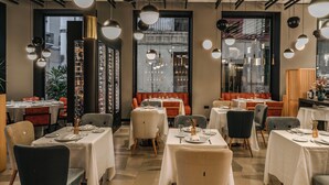 Un restaurant avec des tables dressées, des lampes suspendues et une vue sur l’extérieur par la fenêtre.