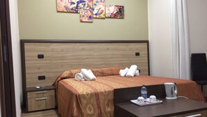 A hotel room with a bed, a desk with a water bottle, and a coffee maker. There are towels on the bed and a nightstand with a lamp. - B&B Duomo Pizzo ApartHotel (Pizzo)