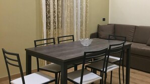 A dining area with a dark wooden table and six chairs, a brown sofa, and a curtain with a pattern. - B&B Duomo Pizzo ApartHotel (Pizzo)