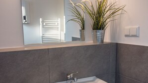 Une salle de bain avec un lavabo blanc, un miroir et deux plantes en pot.