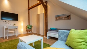 Un salon chaleureux, aménagé dans un style industriel, avec un canapé blanc, une petite table blanche, un téléviseur fixé au mur et un tableau représentant une scène de plage.