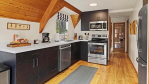 A modern kitchen with dark cabinets, stainless steel appliances, and wooden beams.