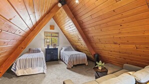 A cozy attic bedroom with two beds, a sofa, and a small table.